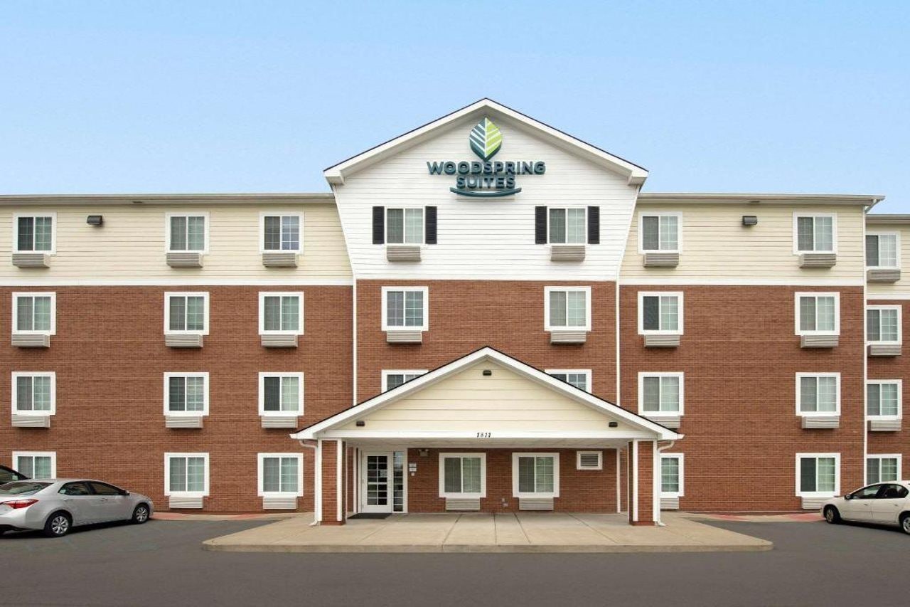 A multi-story hotel with a central entrance, air conditioning units, and a parking lot.