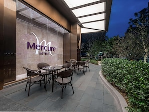 Exterior de un hotel Mercure con mobiliario exterior y fachada de vidrio.