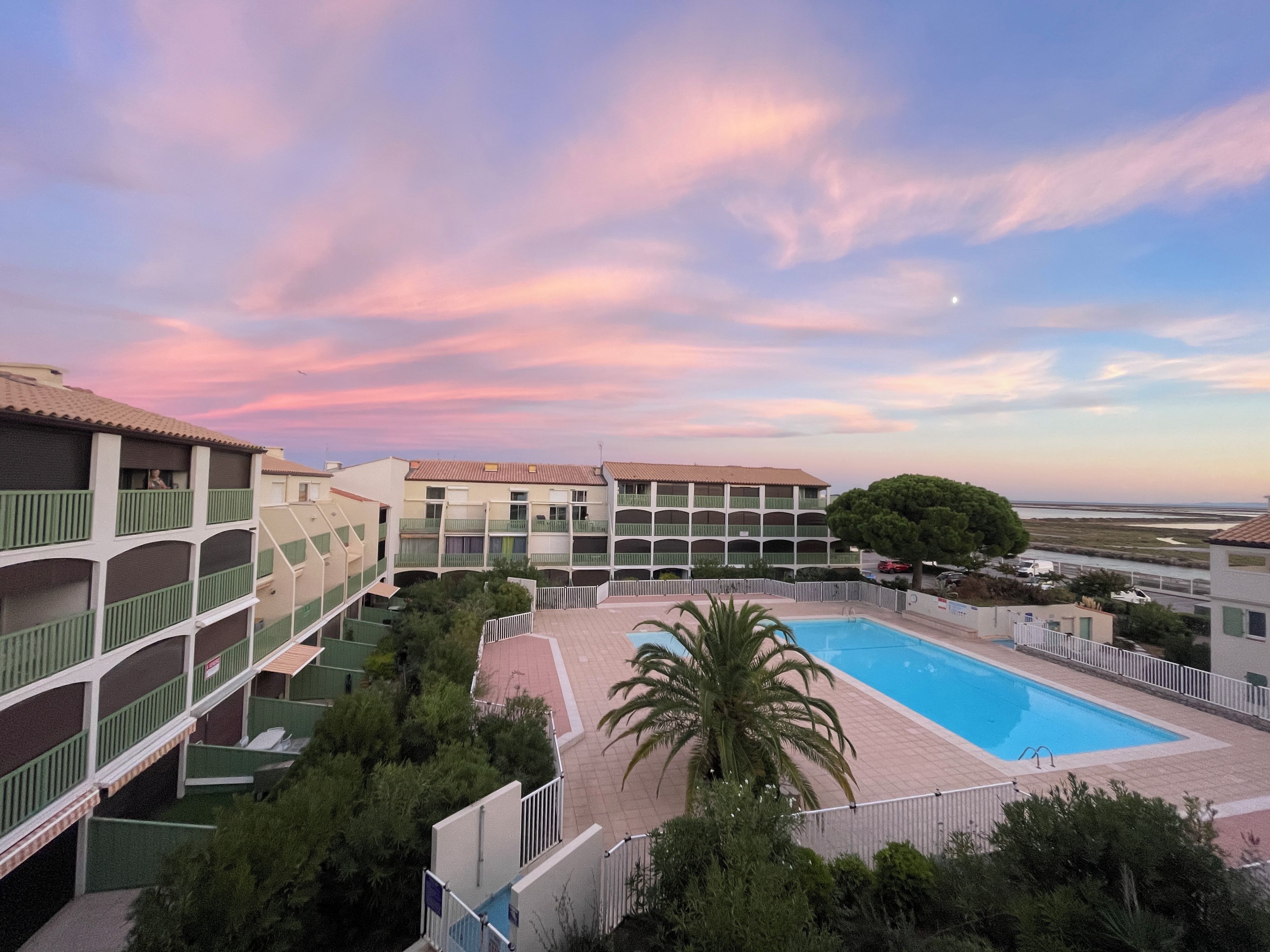 Un hôtel à plusieurs étages doté d’une piscine, entouré de verdure et surplombant un ciel dégagé.