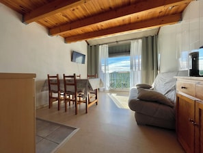 A living room with a wooden ceiling, a sofa, a dining table with chairs, a TV mounted on the wall, and a balcony with a view. - Apartment with a view of the salt flats (Gruissan)