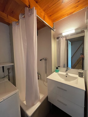 A bathroom with a shower curtain, a sink with a mirror, and a towel rack. - Apartment with a view of the salt flats (Gruissan)