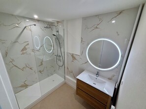 A modern bathroom with a glass-enclosed shower, a round mirror, and a wooden vanity. - A beautiful apartment located just 600 meters from downtown La Rochelle (La Rochelle)