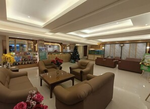 Un vestíbulo de hotel con zonas de estar, un mostrador de recepción y un árbol de Navidad.
