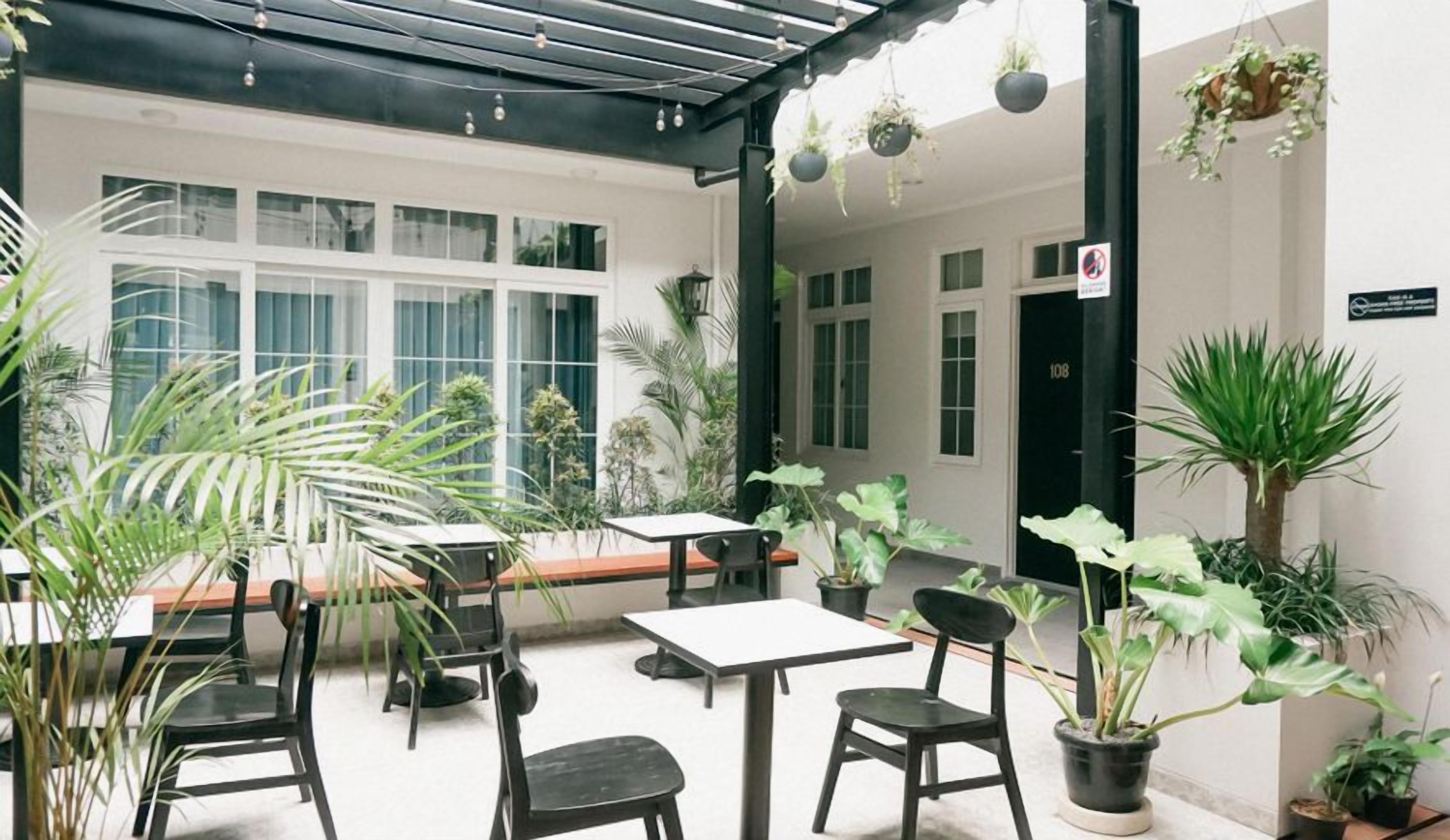 An outdoor seating area with tables and chairs, surrounded by potted plants and a covered section.