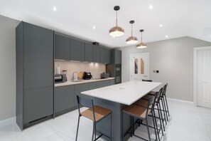 A modern kitchen with grey cabinets, a white island, and pendant lighting. - Willesden Luxe House with Garden (London)