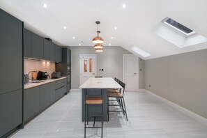 A modern kitchen with a central island, a dining area with a long table, and a skylight. - Willesden Luxe House with Garden (London)