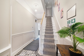 A hallway with a carpeted staircase, a fire exit sign, and a potted plant. - Willesden Luxe House with Garden (London)