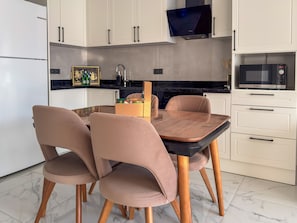 A modern kitchen with a dining table, chairs, cabinets, a television, and a microwave. - Qoople Elize C33 - Cozy 1-bedroom apartment in charming Alanya (Alanya)
