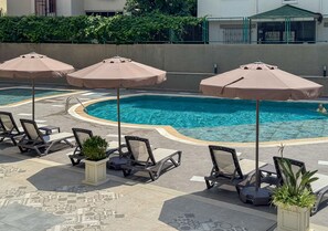 Ein Poolbereich mit Liegestühlen und Sonnenschirmen, umgeben von einer niedrigen Mauer und viel Grün.