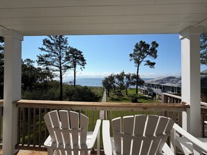 A covered outdoor area with two white Adirondack chairs facing a view of the ocean and a building with a metal roof. - Experience Florida’s Forgotten Coast from your own private waterfront retreat. (Carrabelle)