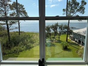 Ein Zimmer mit großem Fenster mit Blick auf eine Wiese, einen Steg und ein Gewässer.