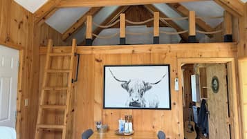 A wooden interior with a lofted ceiling, a framed artwork of a bull, a ladder, and a dining area with a table and chairs.
