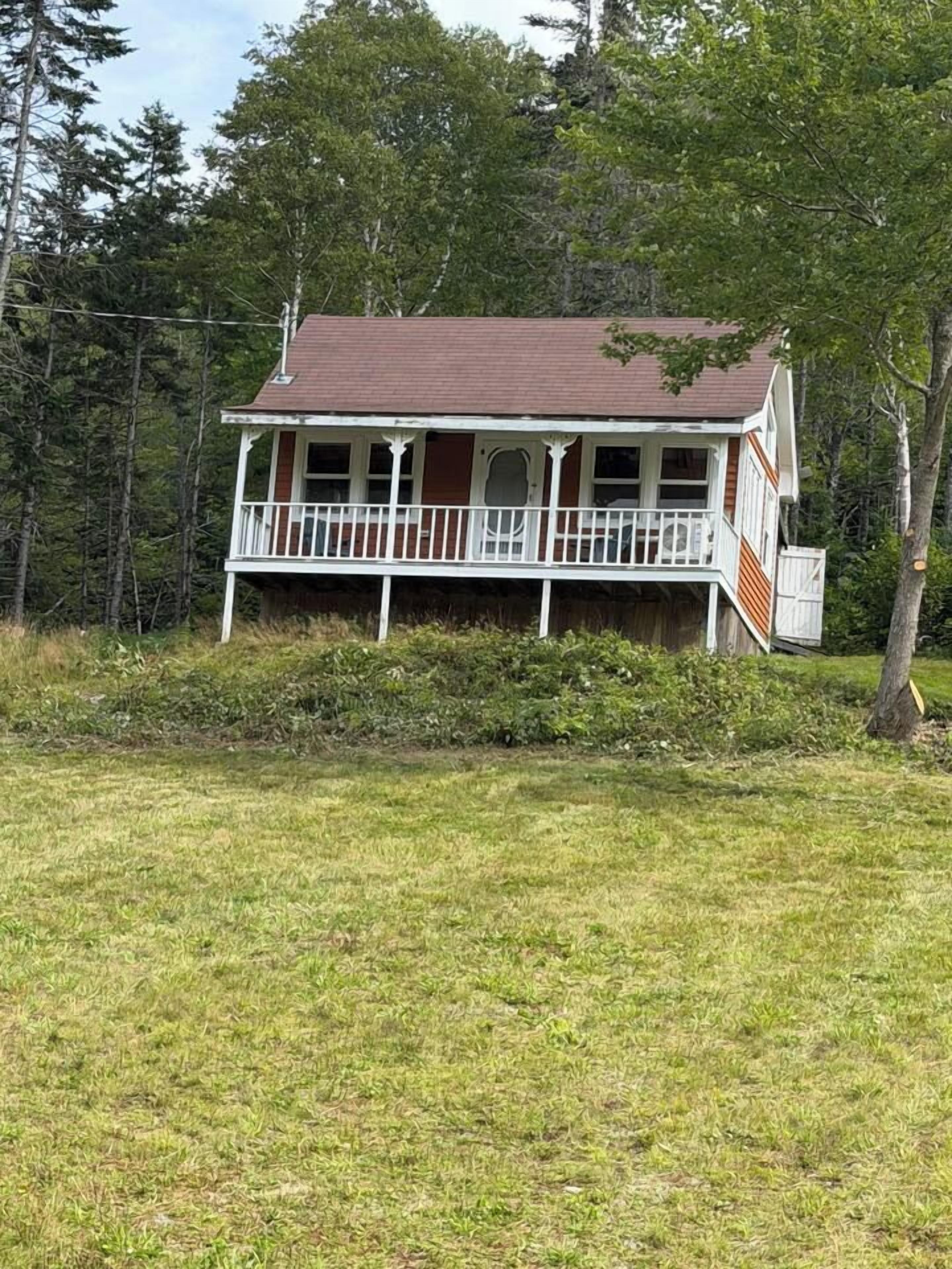 A two-story house with a porch, surrounded by a grassy yard and trees.
