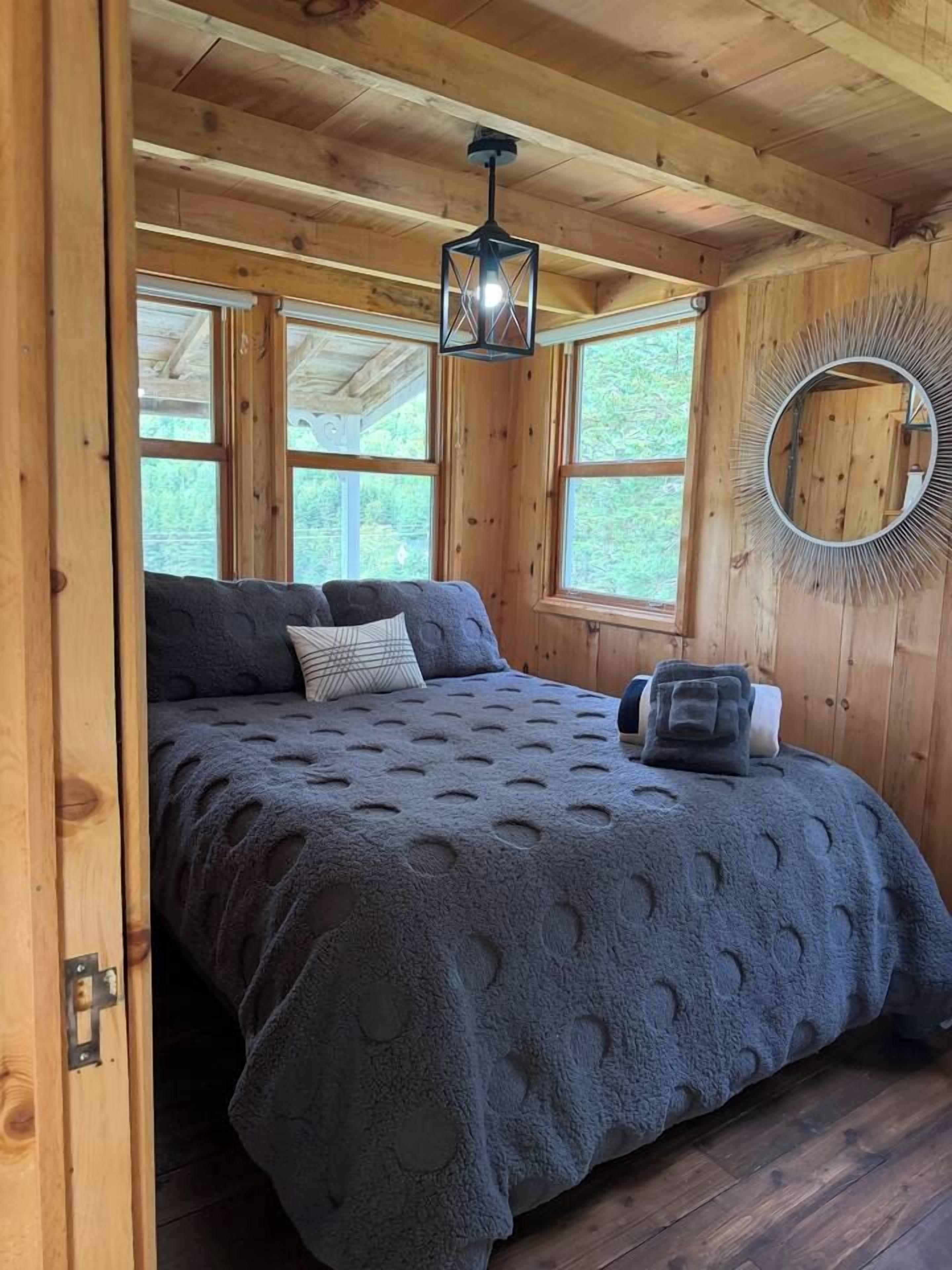 A wooden cabin bedroom with a bed, a hanging lantern, and a circular mirror on the wall.