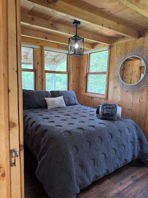 A wooden cabin bedroom with a bed, a hanging lantern, and a circular mirror on the wall.