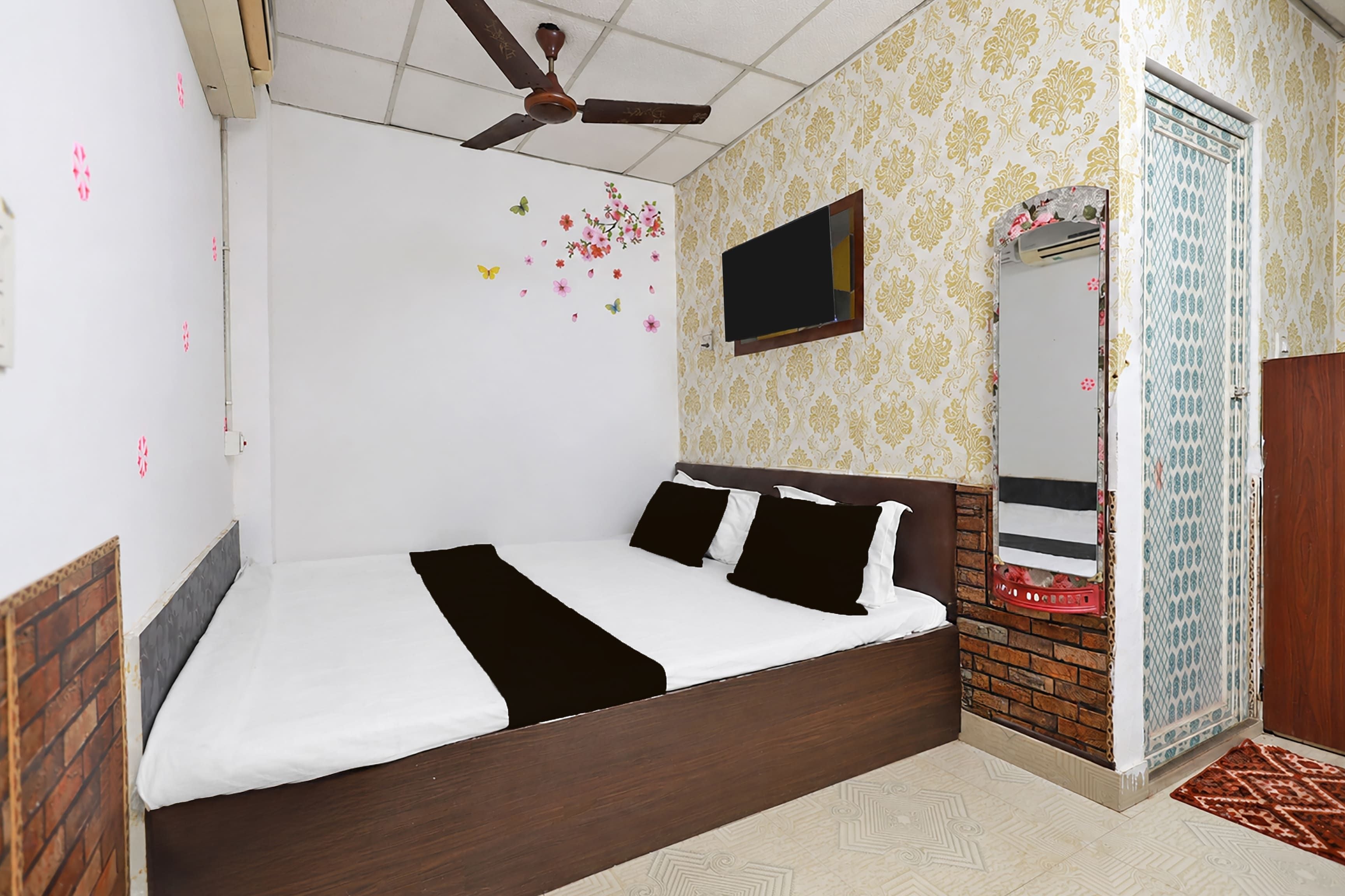 Una camera da letto con un letto, una ventola a soffitto, una TV e una porta con uno specchio.
