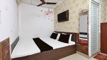 Una camera da letto con un letto, una ventola a soffitto, una TV e una porta con uno specchio.