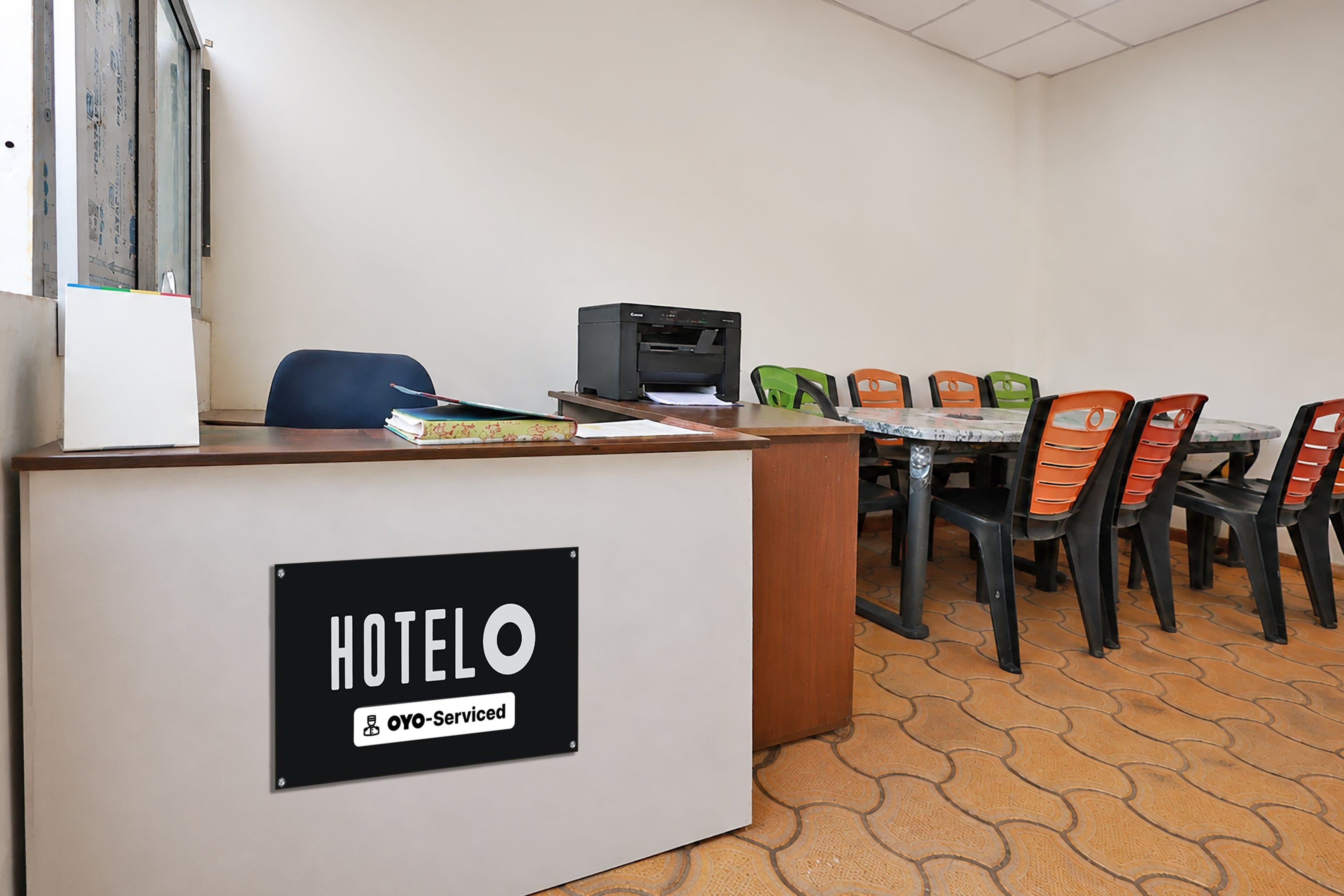 Una reception di hotel con un cartello che indica il servizio OYO. Sono presenti diverse sedie e un tavolo su un pavimento piastrellato.