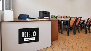 Una reception di hotel con un cartello che indica il servizio OYO. Sono presenti diverse sedie e un tavolo su un pavimento piastrellato.