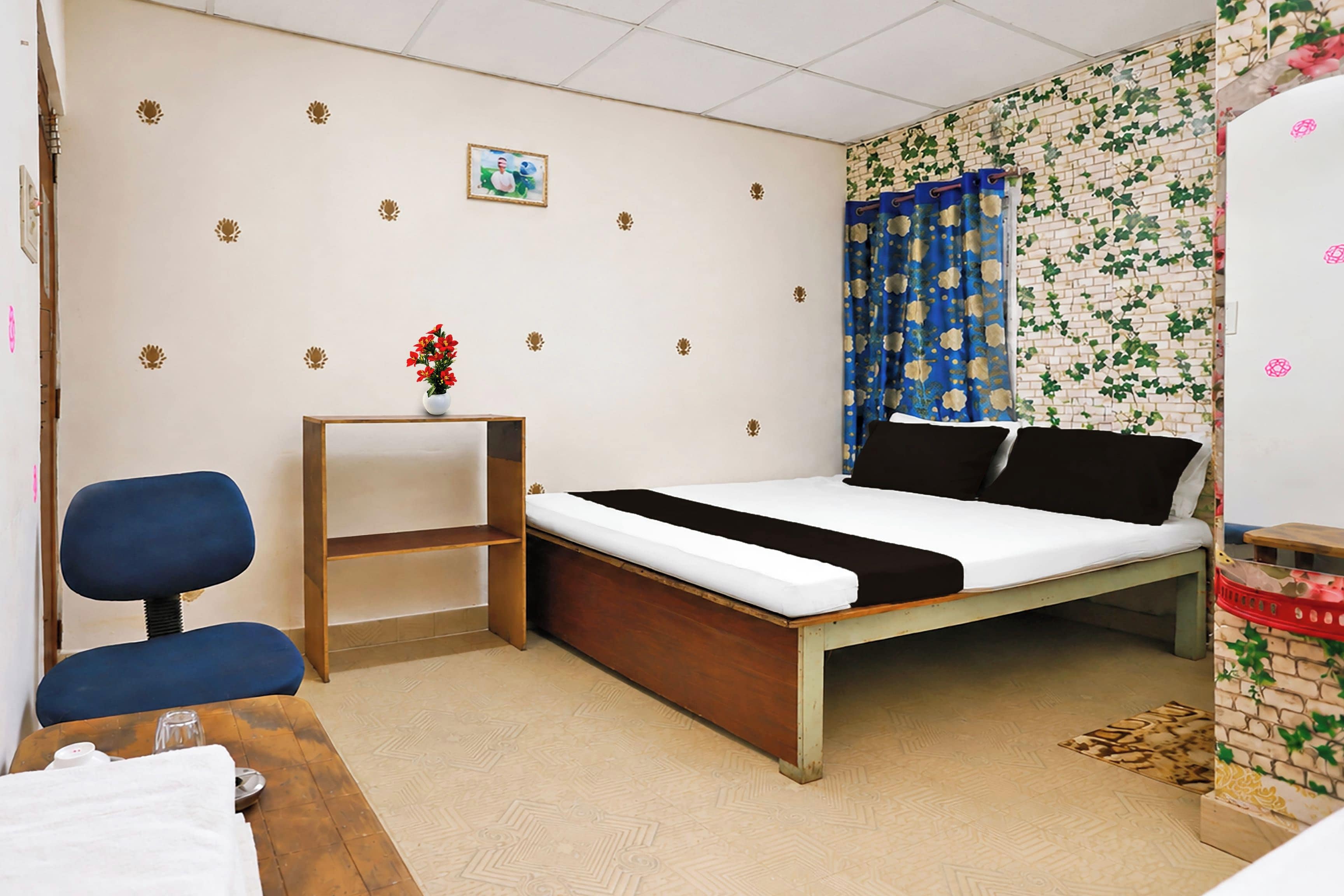 Una cama individual con estructura de madera, una mesita de noche pequeña, una silla y una pared con estampado floral.