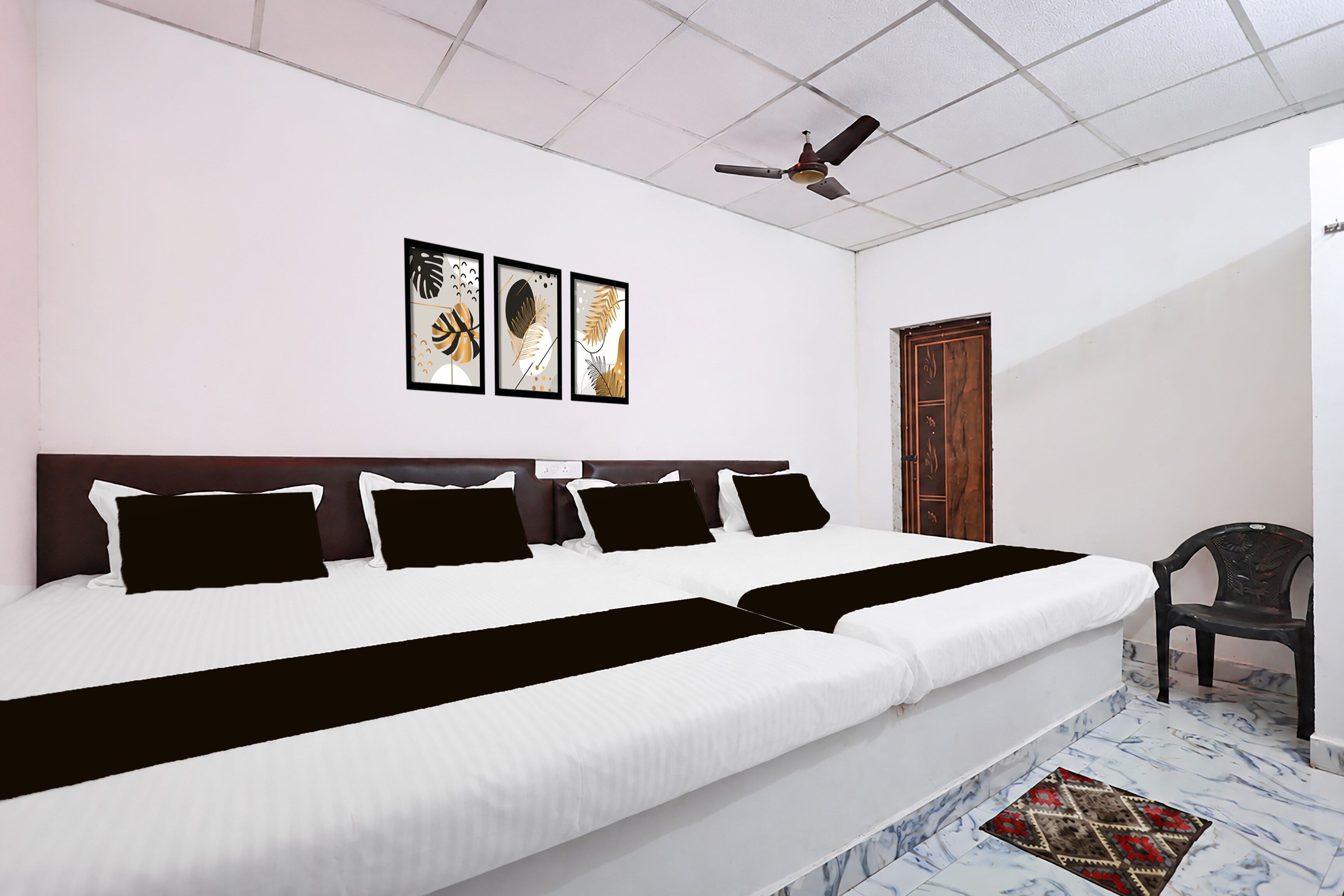 Une chambre d’hôtel avec un grand lit, un ventilateur de plafond et trois œuvres d’art encadrées accrochées au mur.