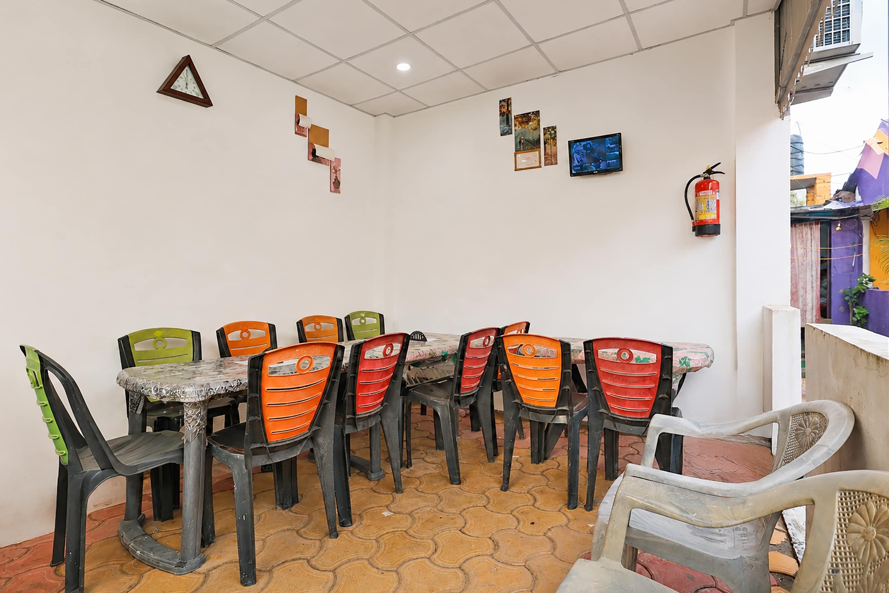 Zona pranzo con pavimento piastrellato, tavolo e sedie, e decorazioni a parete tra cui un orologio, quadri incorniciati e un estintore.