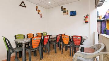 Zona pranzo con pavimento piastrellato, tavolo e sedie, e decorazioni a parete tra cui un orologio, quadri incorniciati e un estintore.