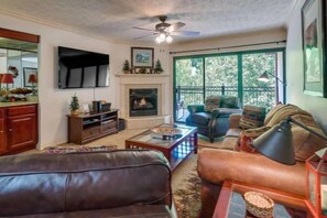 A living room with a fireplace, leather sofas, a TV, and a large window. - Creek & Mountain Views, Free Tickets to Area Attractions (Gatlinburg)