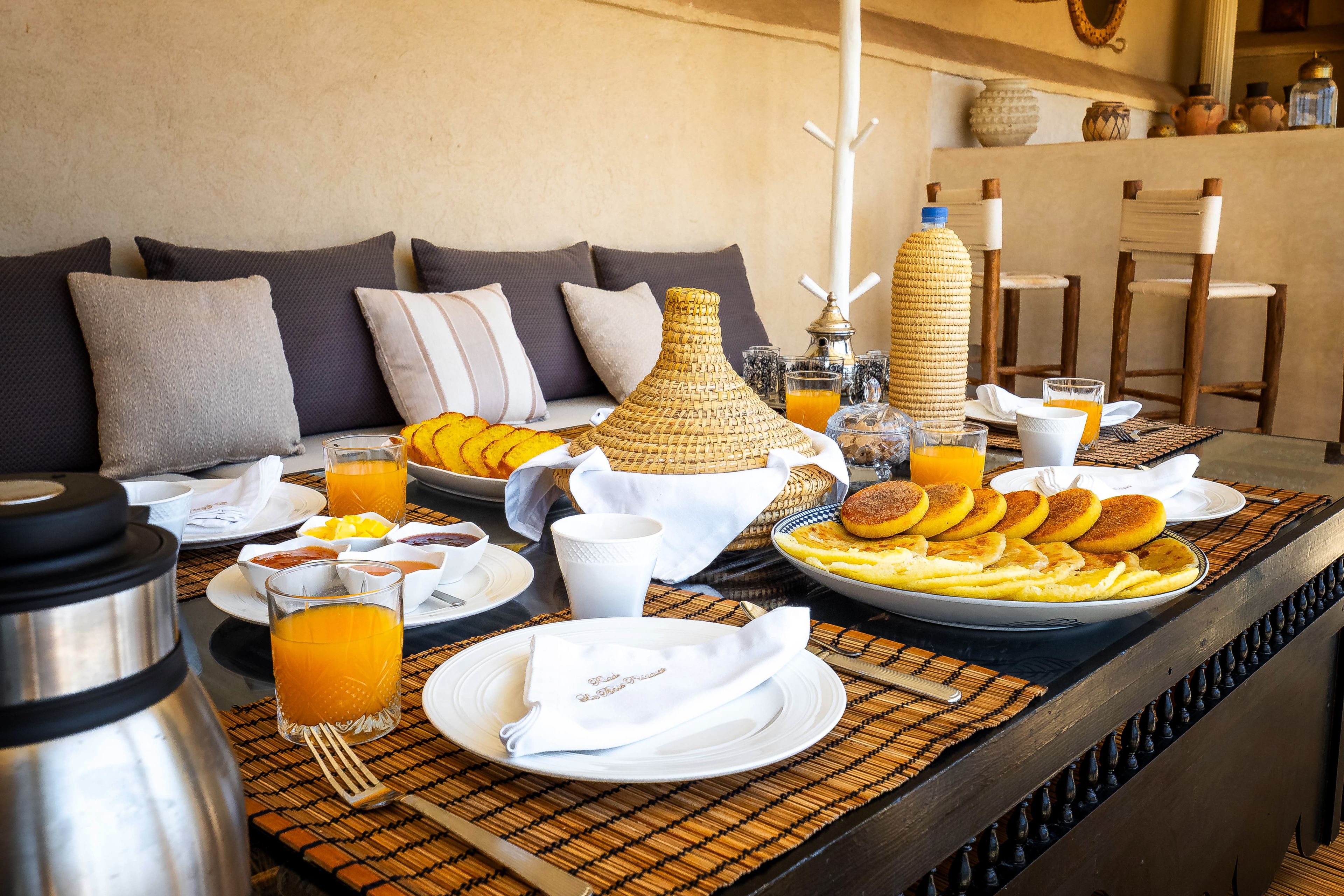 Un bufé de desayuno con diversos platos, una cafetera y una botella de zumo de naranja sobre una mesa.