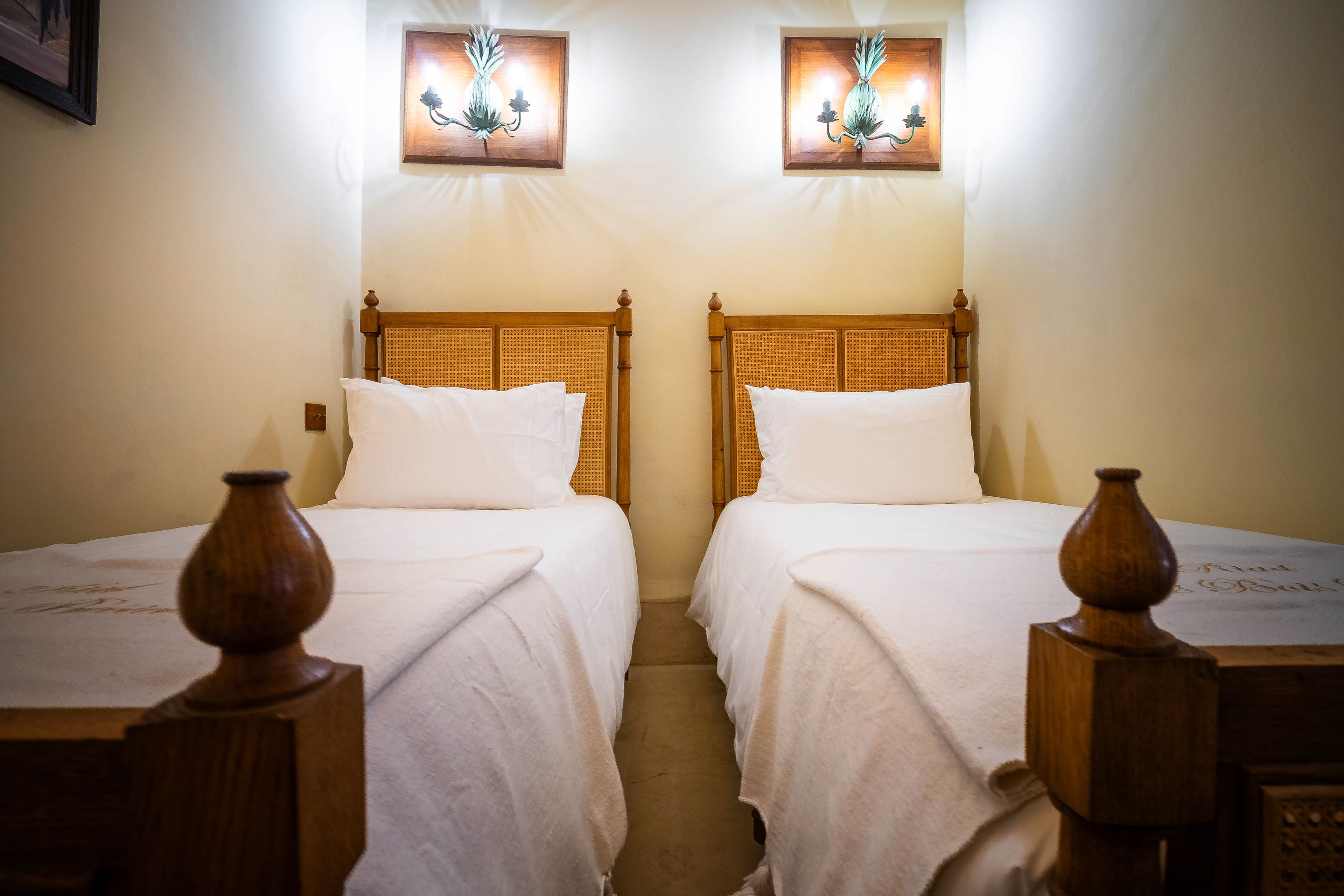 Dos camas individuales con cabeceros de madera y ropa de cama blanca, acompañadas por apliques de pared con diseños florales.
