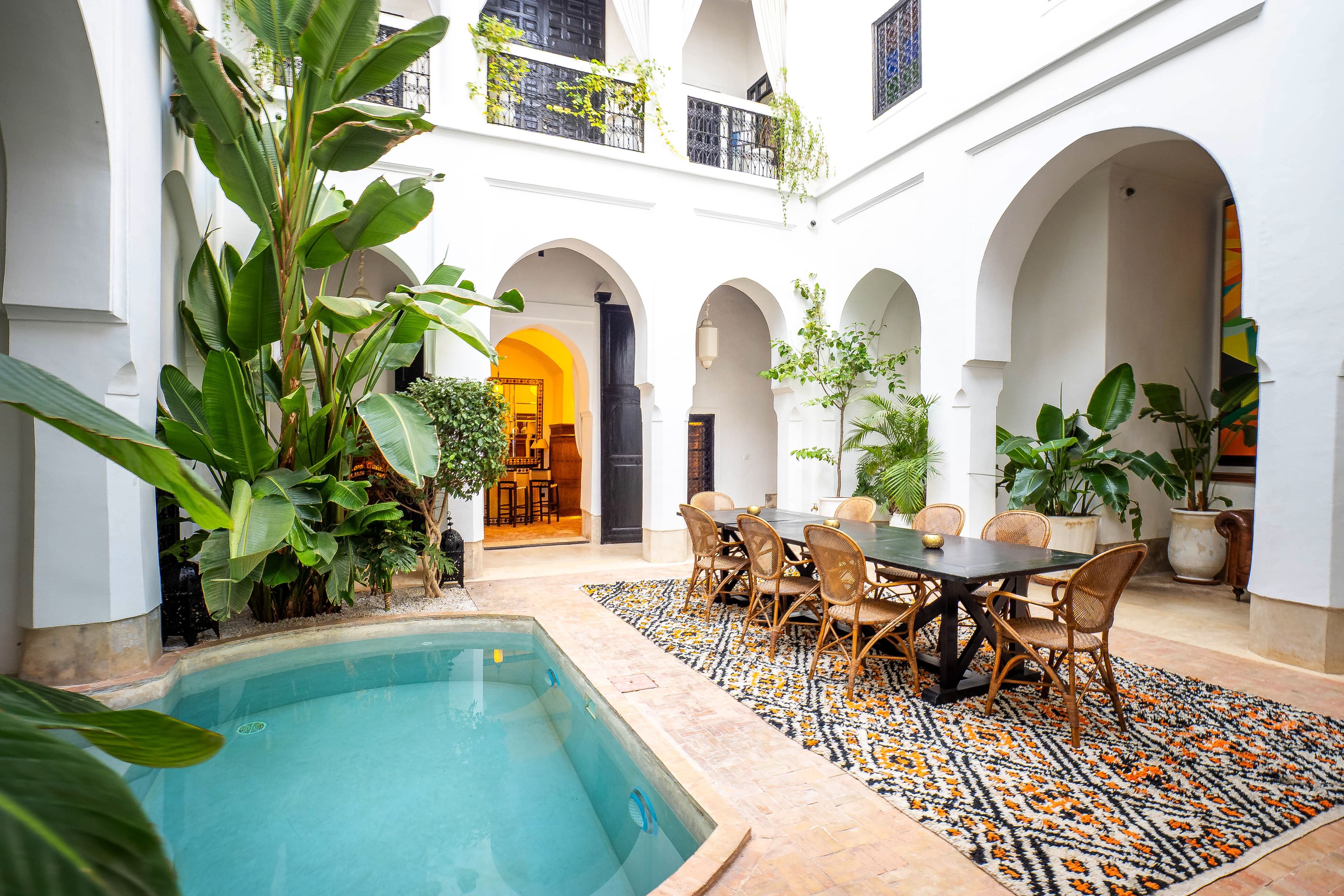 Un patio con piscina, zona de comedor y varios arcos.
