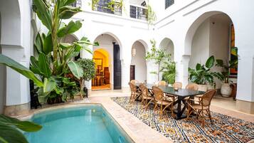 Un patio con piscina, zona de comedor y varios arcos.