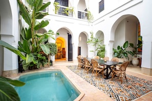 Pátio com piscina, área de refeições e várias arcadas.