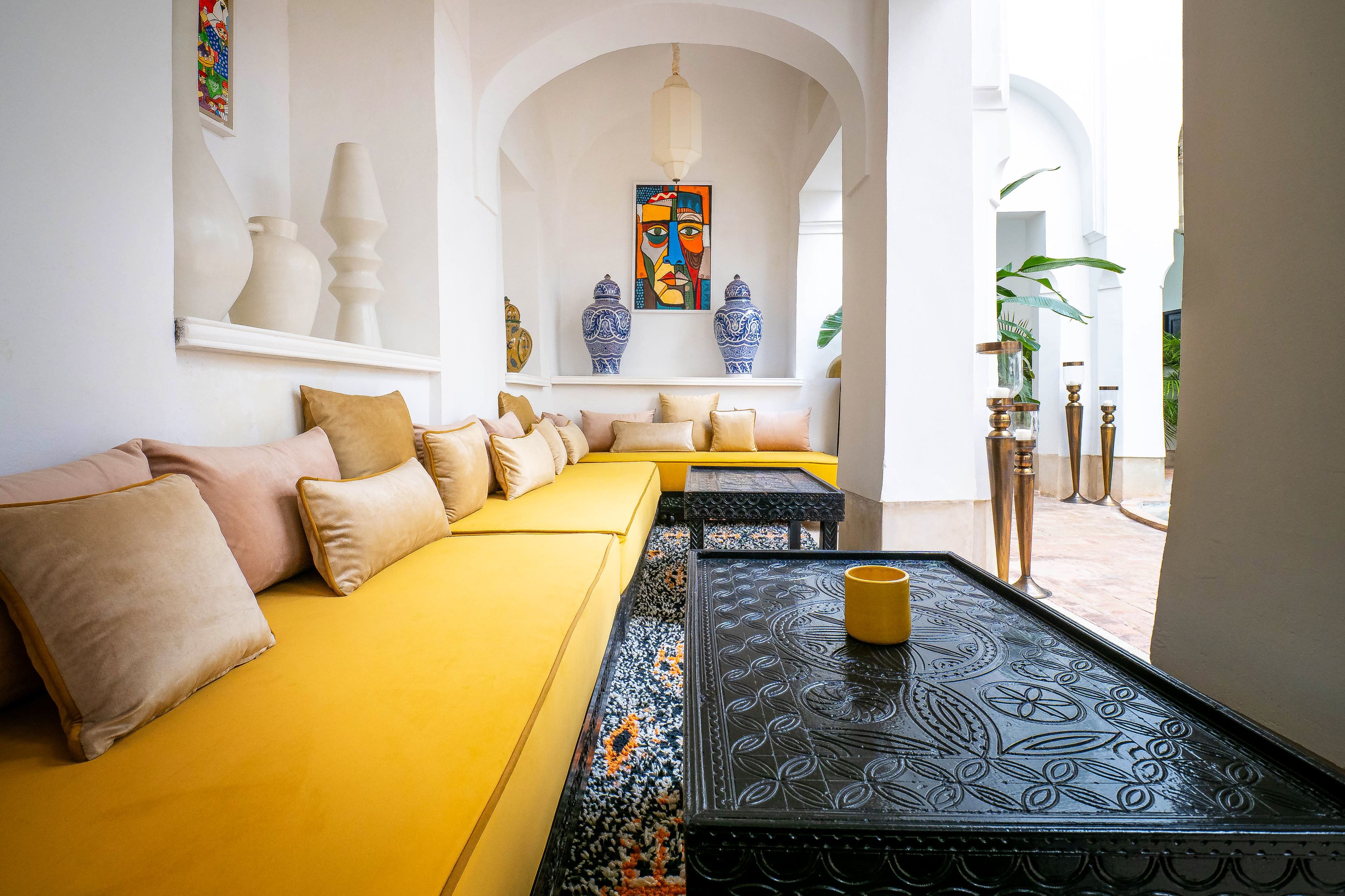 Una sala luminosa con un sofá amarillo, una mesa de centro estampada y jarrones decorativos.