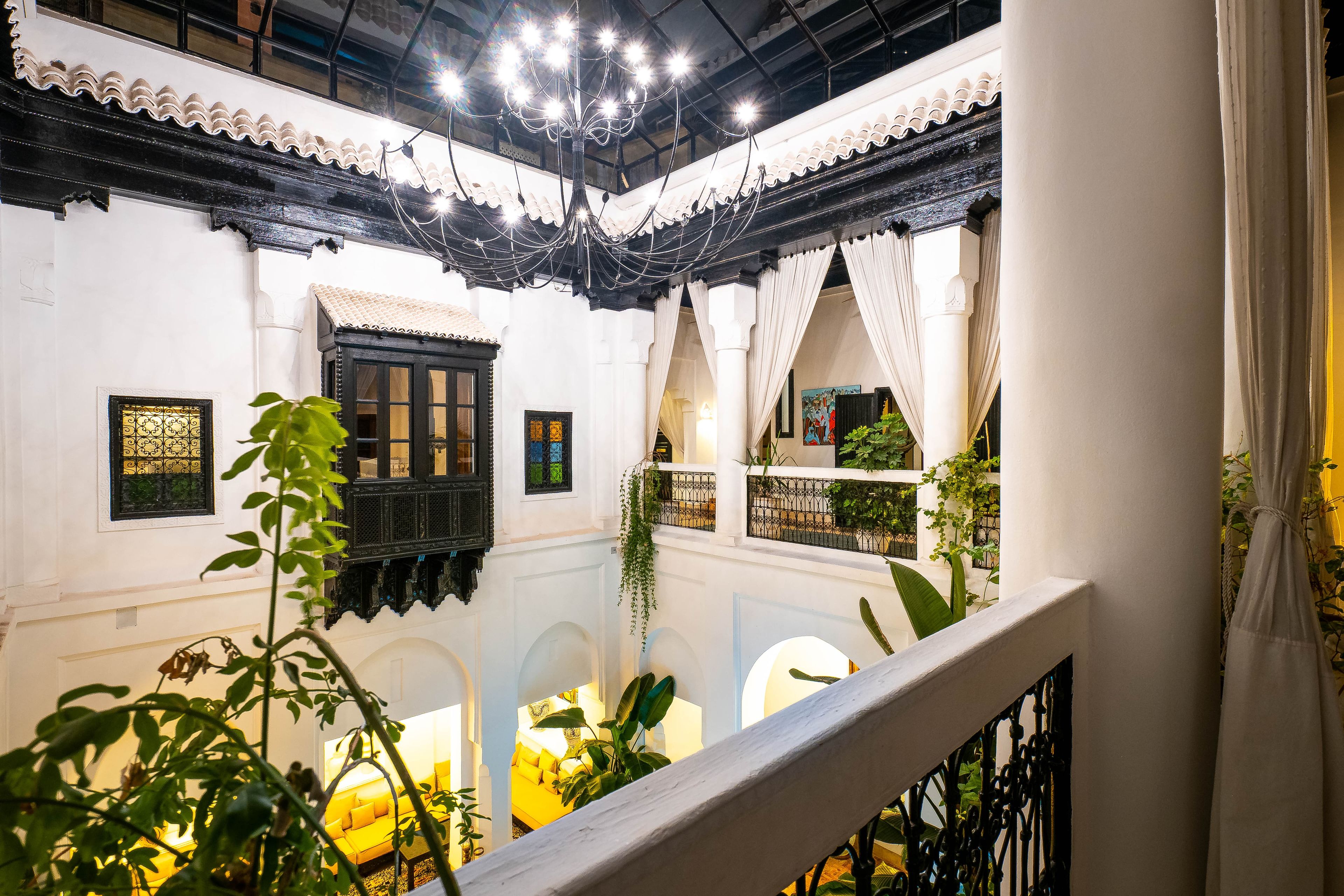 Un patio con paredes blancas, ventanas de marco negro y un balcón con plantas.