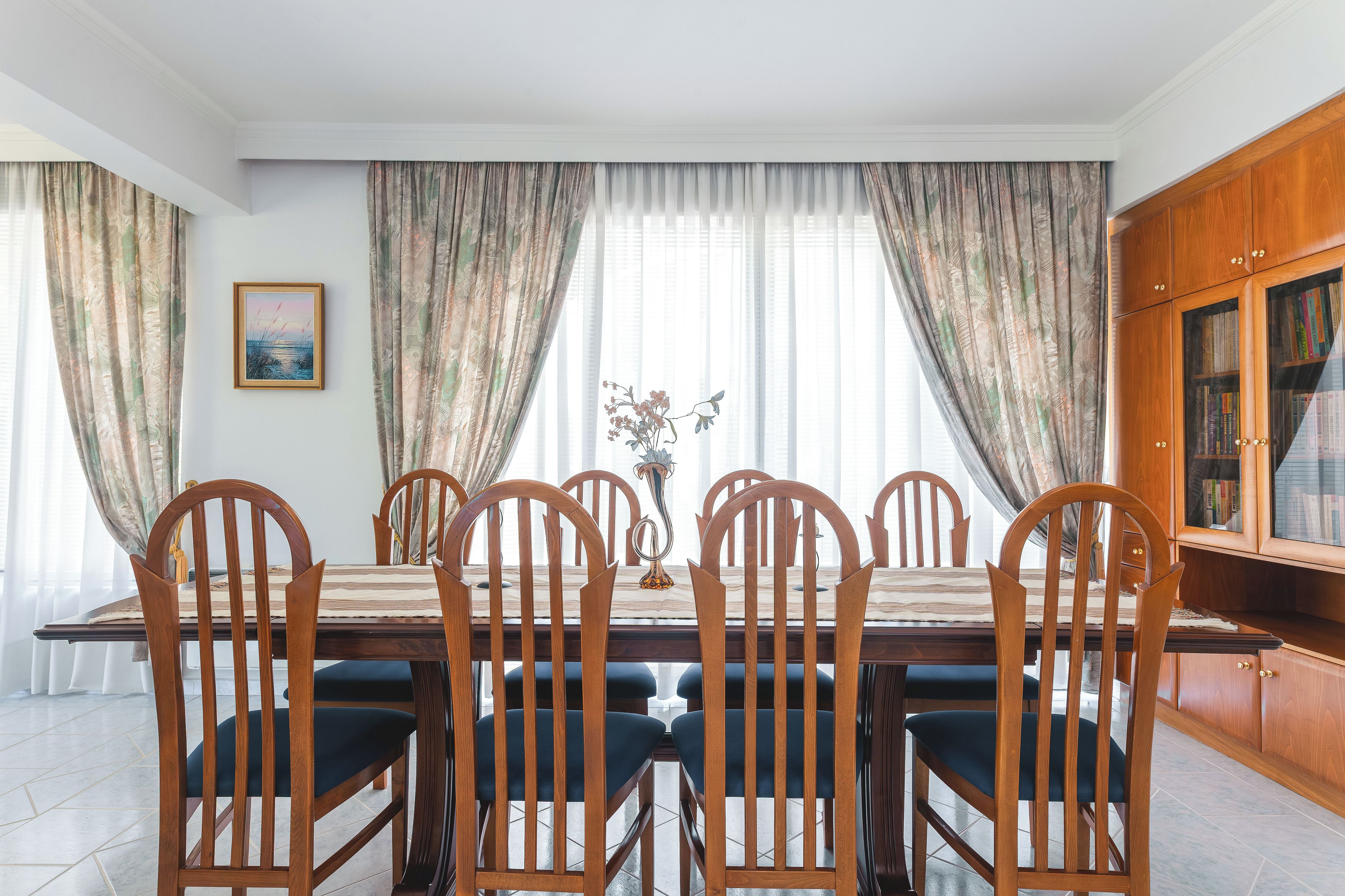 A dining area with a wooden table and chairs, a vase with flowers, and a bookshelf.