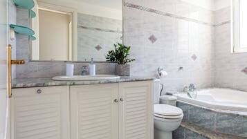 Een badkamer met een marmeren wastafel, toilet en bad.