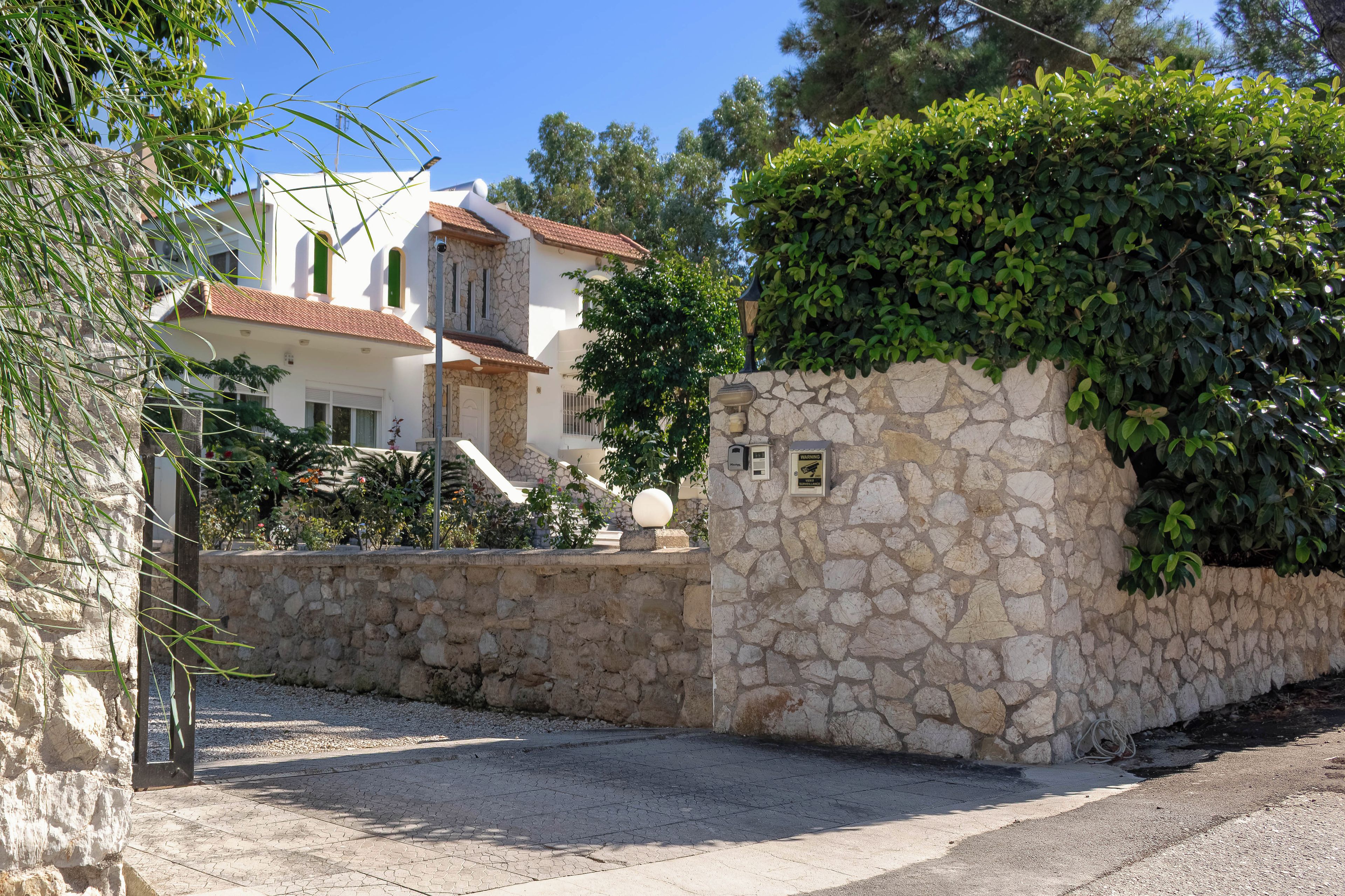 A stone wall with a warning sign, a paved area, and a building with a tiled roof.