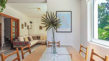 Ein Essbereich mit Holztisch, Stühlen, einer Tischdecke aus Spitze, einer Vase mit Pflanze und einem gerahmten Bild an der Wand.
