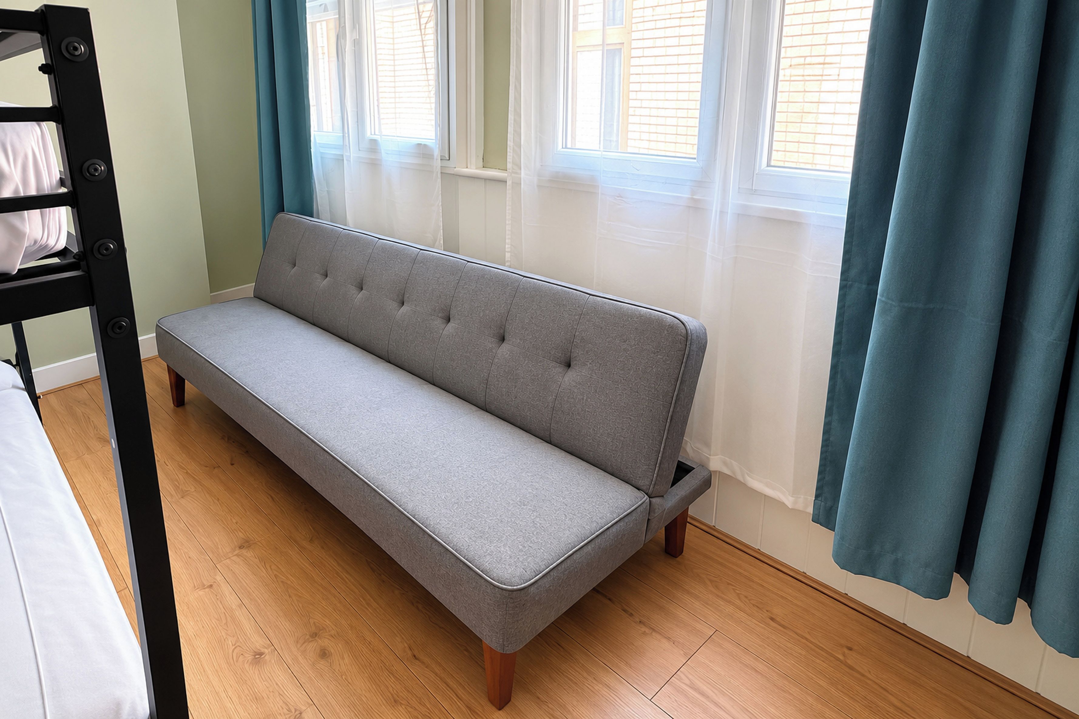 A room with a grey sofa, wooden flooring, a bunk bed, and a window with curtains.