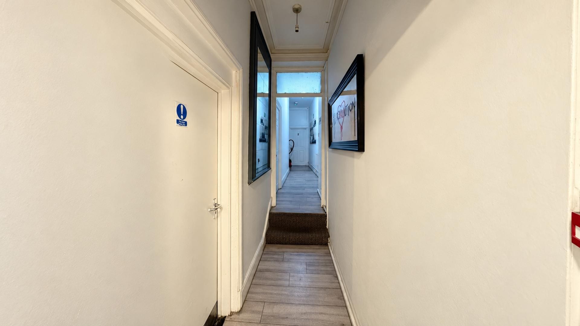 A narrow hallway with a door on the left and a framed picture on the right.