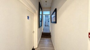 Un corridoio stretto con una porta a sinistra e un quadro appeso a destra.