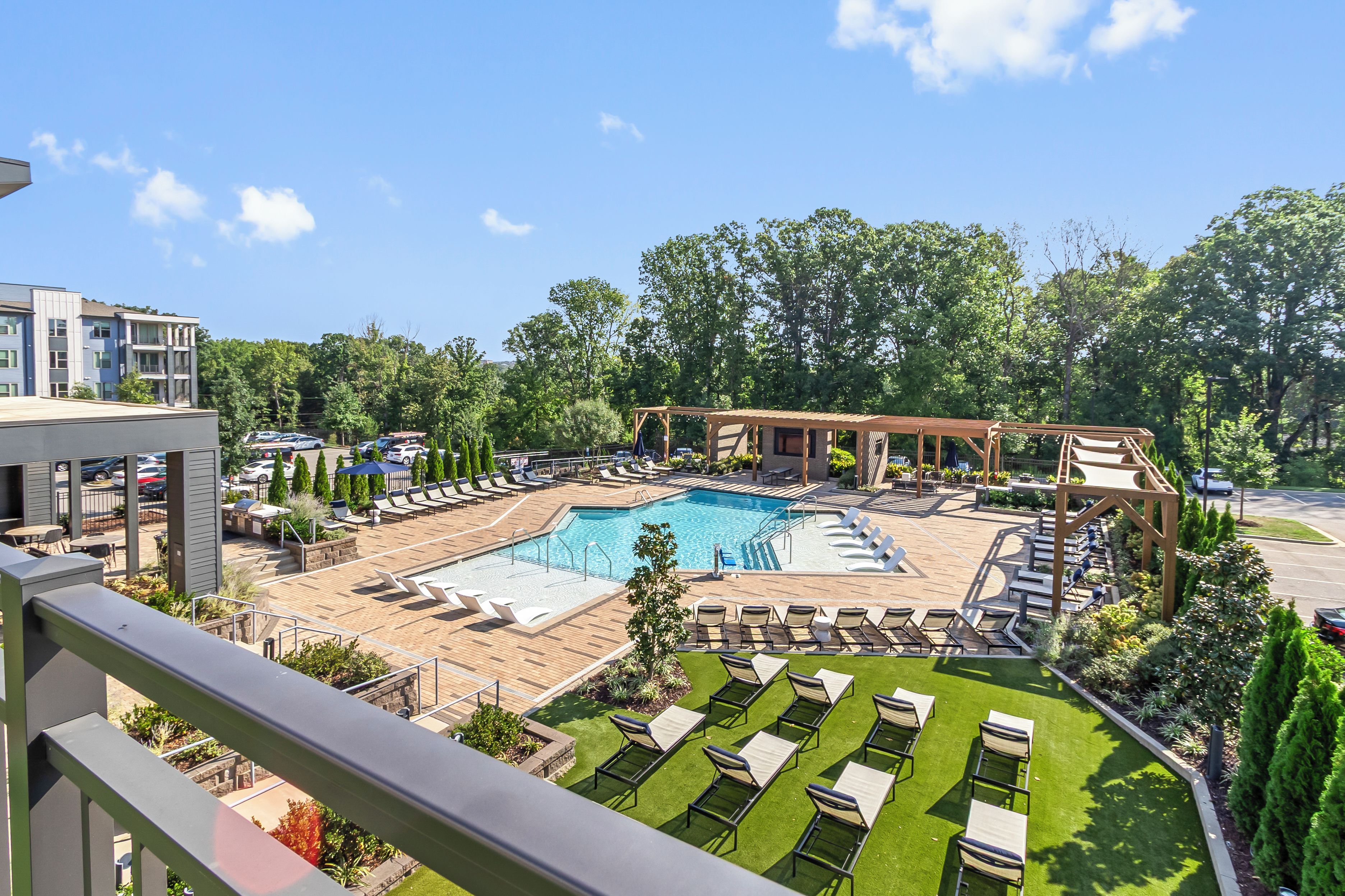 A pool area with lounge chairs, a wooden deck, and a view of a residential building.
