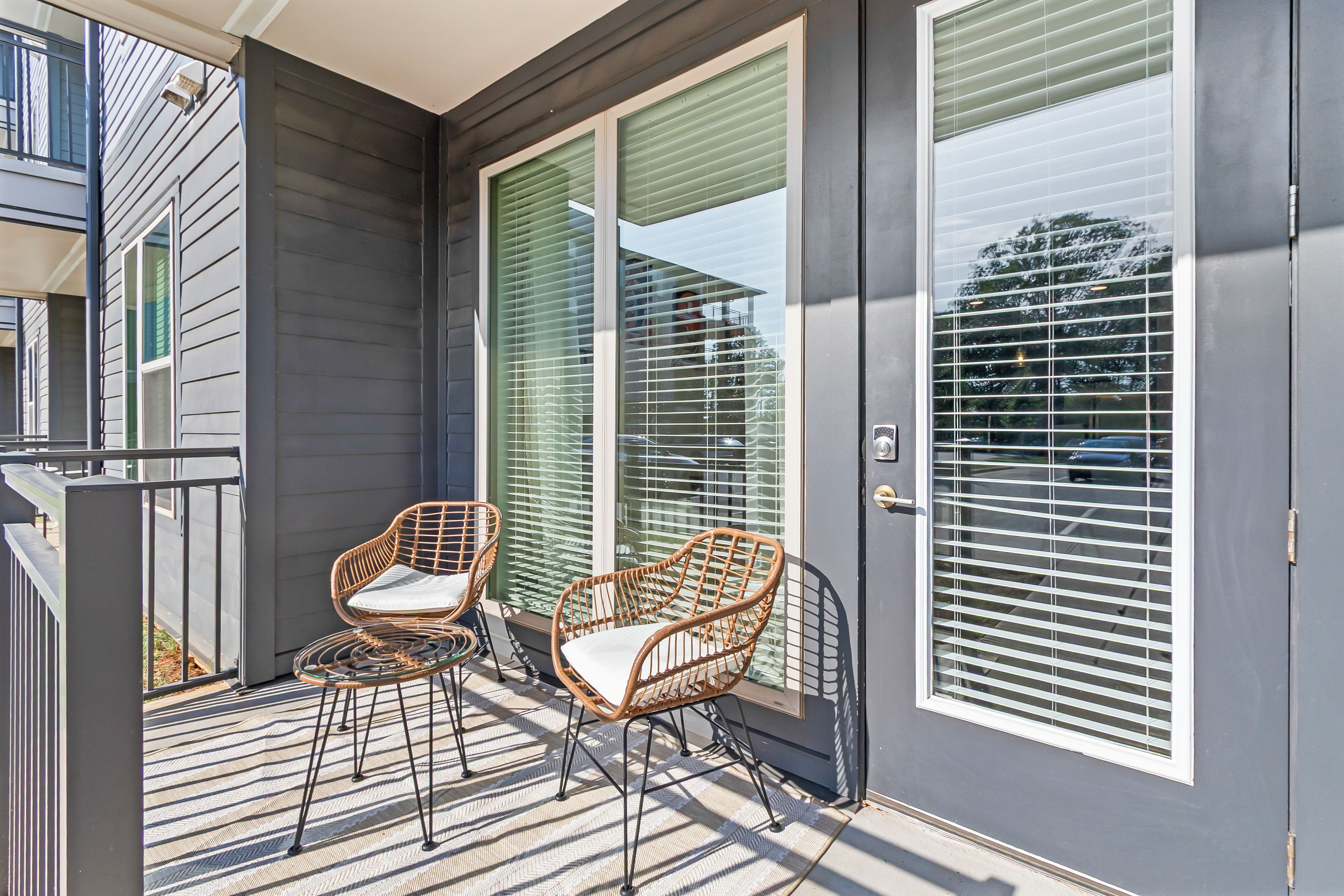 A covered outdoor area with two wicker chairs and a small table, a sliding glass door, and a view of a street with cars.