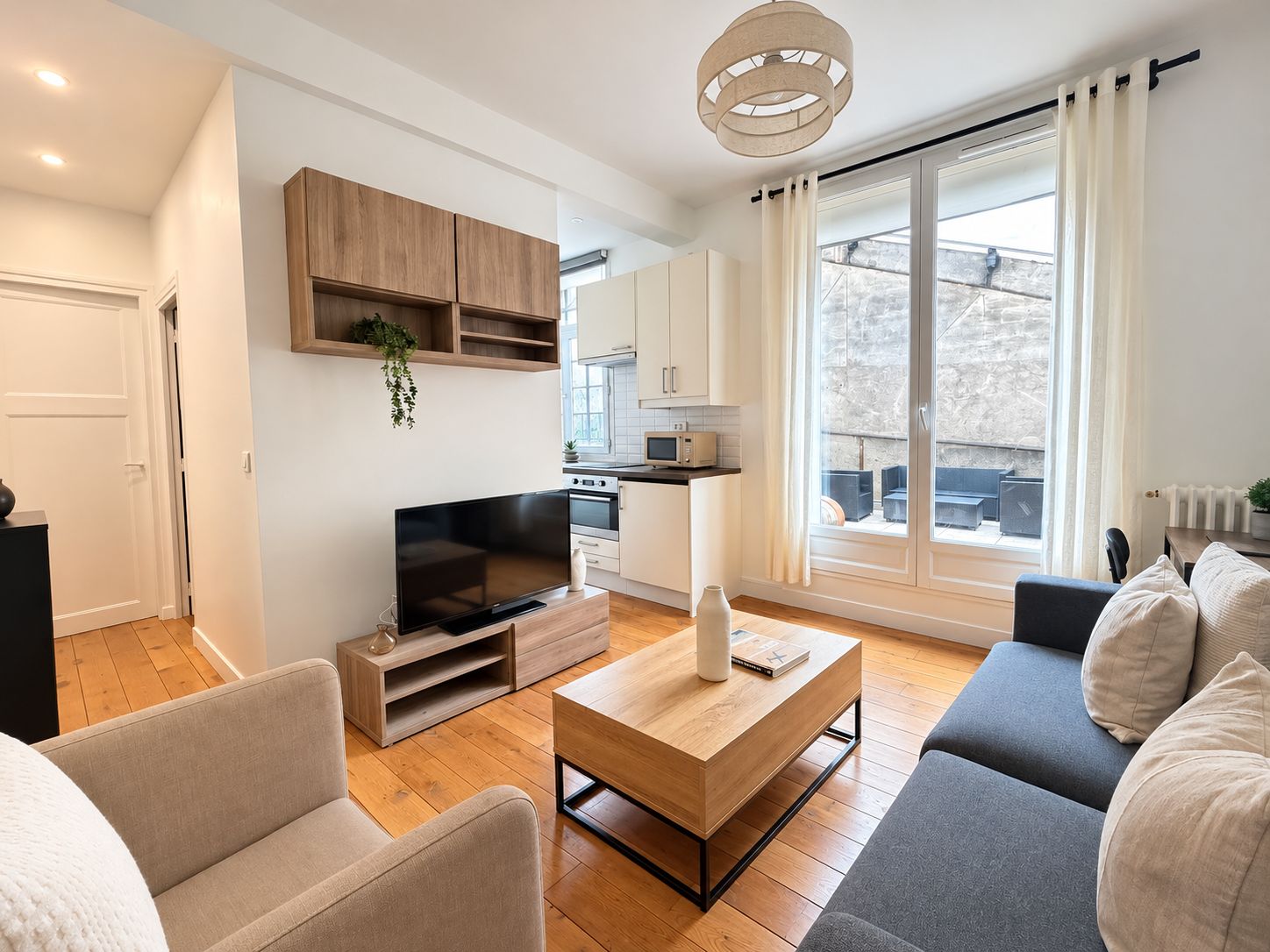 A modern living room with a flat-screen TV, wooden cabinets, a dining area, and a large window with curtains.