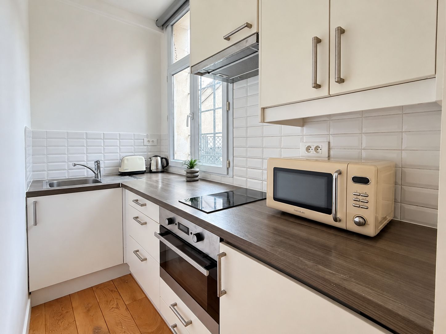 A modern kitchen with white cabinets, a dark countertop, a built-in oven, a microwave, and a window providing natural light.