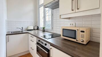 A modern kitchen with white cabinets, a dark countertop, a built-in oven, a microwave, and a window providing natural light.