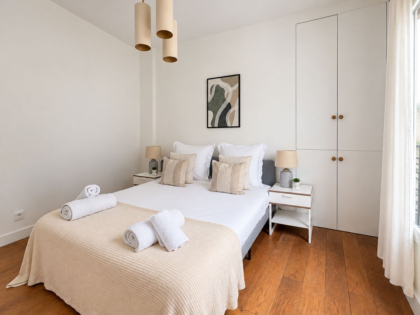 A hotel room with a large bed, two bedside tables, a wardrobe, and a window with curtains.
