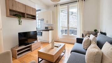 A modern living room with a flat-screen TV, a wooden coffee table, a grey sofa, and a kitchen in the background.