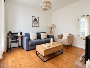 A modern living room with a grey sofa, a wooden coffee table, a desk with a chair, a floor lamp, and a large mirror. - Magnifique Appartement Levallois Perret (Levallois-Perret)